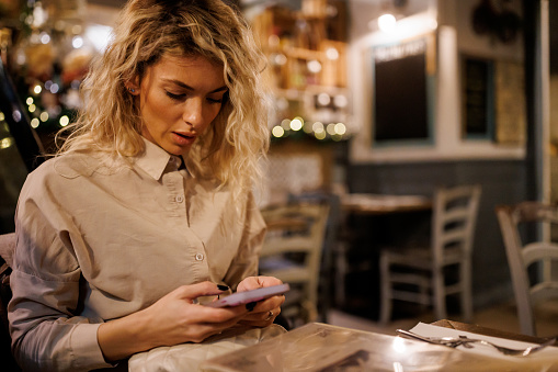 Beautiful young woman texting on mobile phone at cafe in the evening