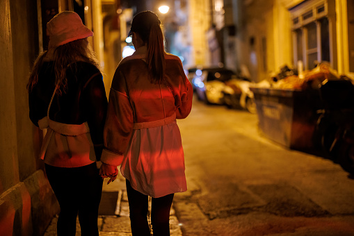 Back view of lesbian couple holding hands and walking in city at night