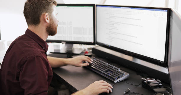 istock Young businessman working on a computer with multiple monitors at his desk 1464659255