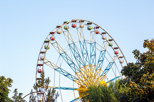 High carnival Ferris wheel in the amusement park in summer spinning against the blue sky.