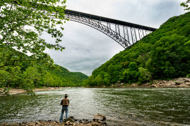 West Virginia, USA - May 24, 2022: An adult man fishes in the river, 1000 feet below the New River Gorge Bridge on a summer day, Fayetteville.