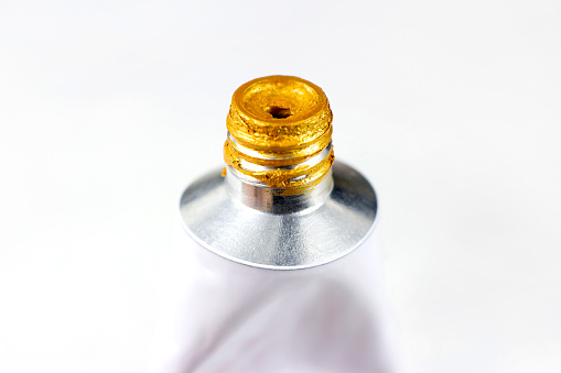 Metal acrylic tube with golden paint for drawing close up on white background with copy space.