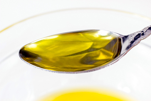 Yellow organic olive oil in the spoon on light background close up.