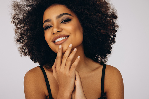 Closeup of a young, stylish, and edgy black woman standing or posing against a grey studio background alone. One confident, trendy and sassy female with an afro looking powerful and wearing makeup