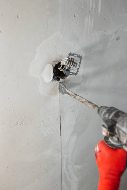 istock Builder electrician makes a hole puncher in a concrete wall for installation of electrical cables 1464666814