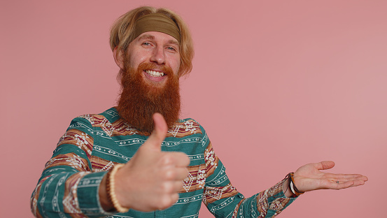 Hippie man showing thumbs up and pointing empty place advertising area for commercial text promotion