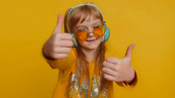 Photo of Happy preteen child girl kid listening music via headphones and dancing disco fooling around