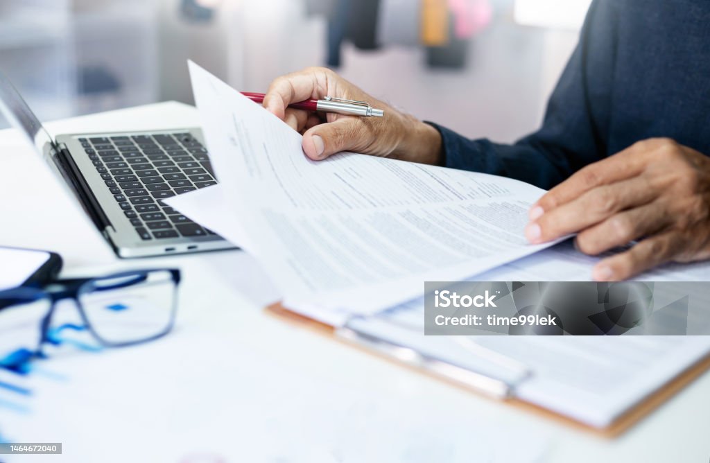 Бизнес и финансы. Азиатский бизнесмен просматривает документы и отчеты на рабочем месте в офисе с ноутбуком. Юридический эксперт, профессиональный юрист, читает и проверяет финансовые документы или договор страхования. Фотография документа.