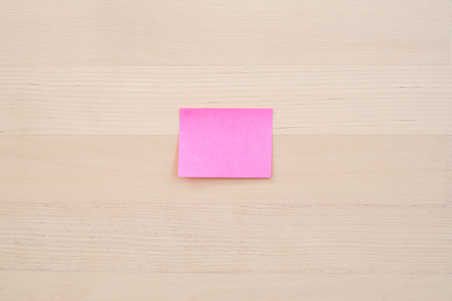 Blank pink sticky note on desk, selective focus.