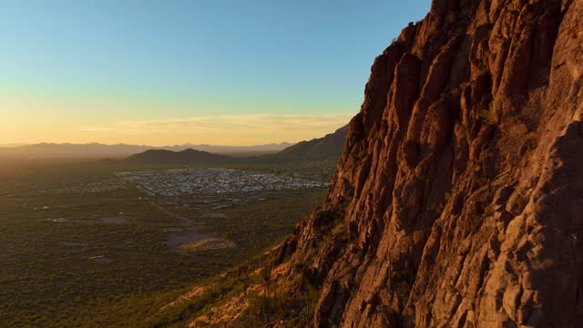 Cinematic aerial shot passing rocky peaks of desert mountains revealing Tucson Arizona, into the sun, POV drone