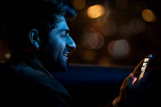 Happy man using mobile phone on back seat of car Young man messaging on mobile phone while sitting on back seat of car at night happy car asian stock pictures, royalty-free photos & images
