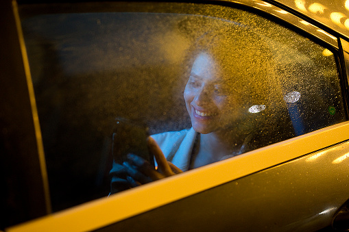 Young woman messaging on mobile phone while sitting on back seat of car at night