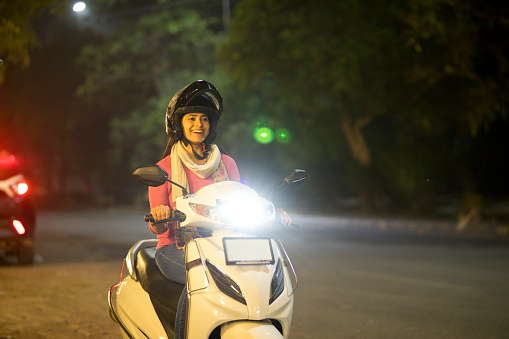 Smiling woman enjoying riding a scooter with helmet at night