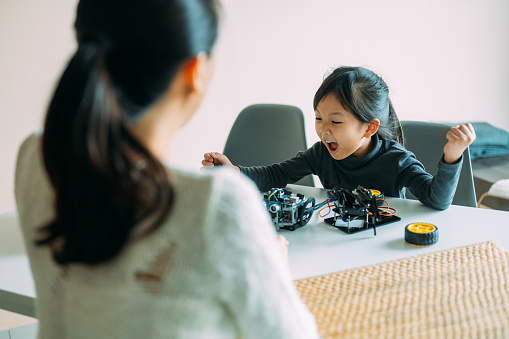 Young Asian girl building robot toy together with her mother at living room