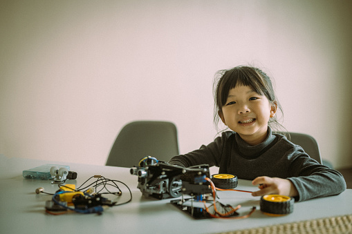 Portrait of an Asian Chinese girls enjoy making and fixing her electrical robot car at home. Looking at camera.