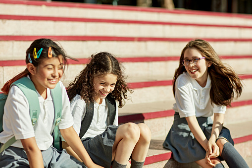 Front view of 9 and 11 year old classmates wearing uniforms, sitting on campus staircase, and interacting.