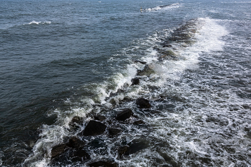 The Baltic Sea water washes over a breakwater made of stones and forms agitated and calm water.