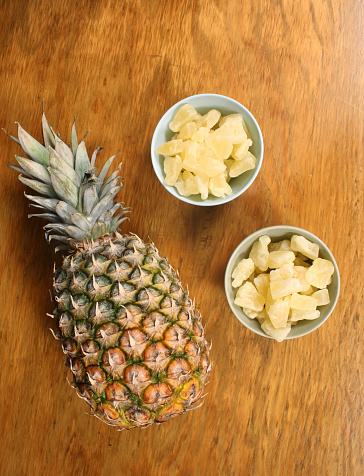 A vertical shot of fresh pineapple and dried ones in the bowls on the wooden surface