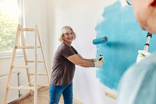 Happy senior couple communicating while painting their walls during home renovation process.