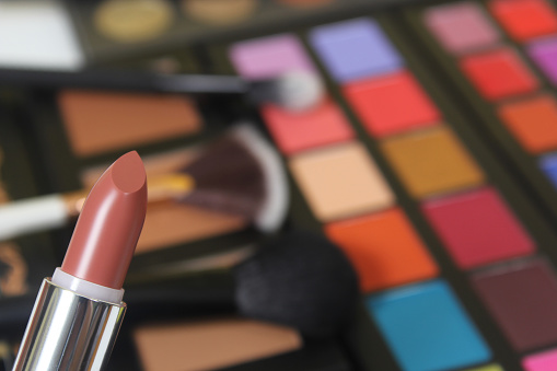 A selective shot of brown lipstick and brightly coloured cosmetic pigmented eye shadows on the background