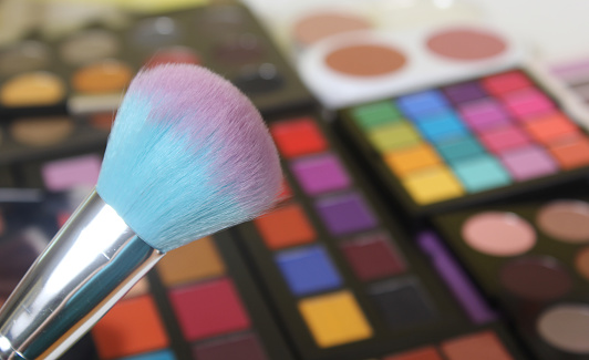 A selective shot of a makeup brush and brightly coloured cosmetic pigmented eye shadows on the background