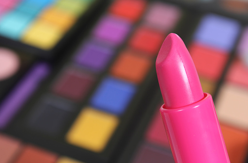 A selective shot of pink lipstick and brightly coloured cosmetic pigmented eye shadows on the background