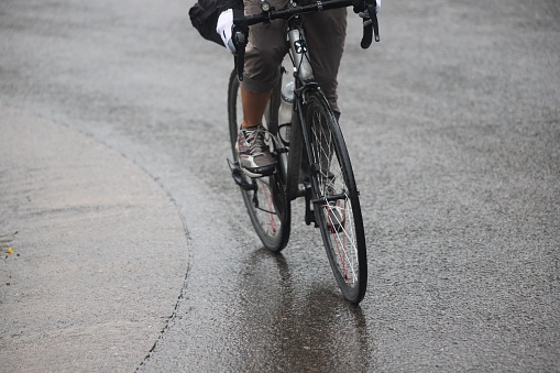Bogota, Colombia – November 23, 2019: A closeup of a man riding a road bicycle on a wet asphalt under a light rain