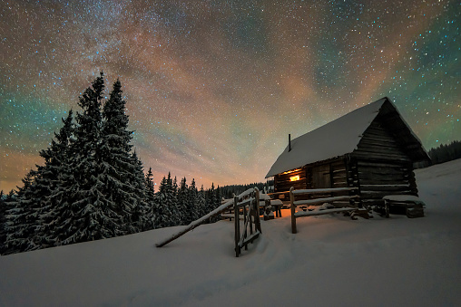 Beautiful winter landscape with a starry sky. The light in the cabin in the mountains