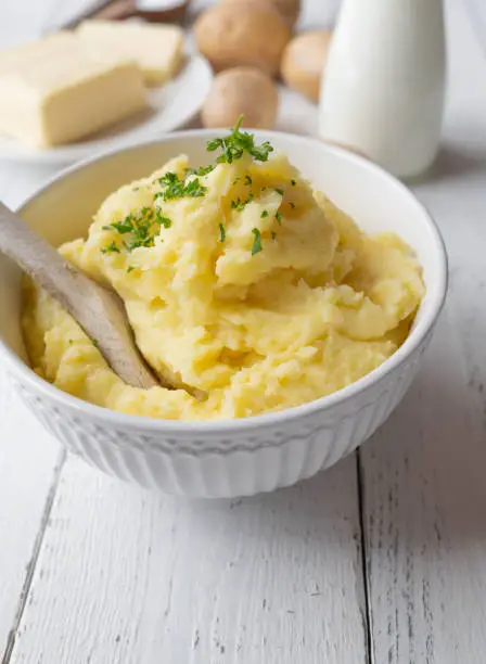 Homemade fresh cooked mashed potatoes or potato puree. Served in white bowl with wooden spoon on white table background. Closeup and low angle view with copy space