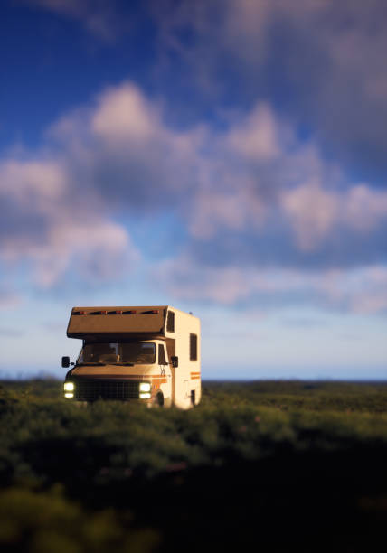 istock Motor home with lit headlights in countryside under a blue cloudy sky. 3D render. 1464698014