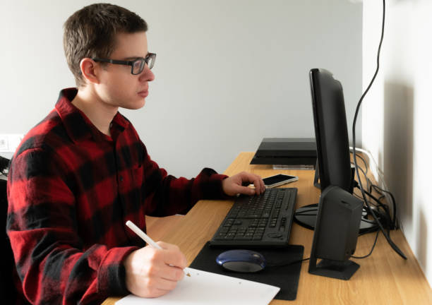 istock Spanish Caucasian teenager in an online class with his computer and taking notes, indoors 1464698582