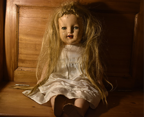 A closeup of a creepy old toy with disheveled hair sitting on a wooden chair