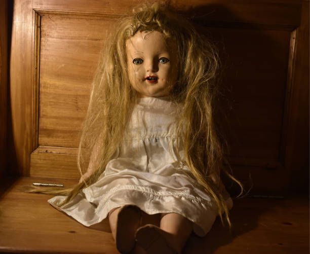 Closeup of a creepy old toy with disheveled hair sitting on a wooden chair A closeup of a creepy old toy with disheveled hair sitting on a wooden chair creepy doll stock pictures, royalty-free photos & images