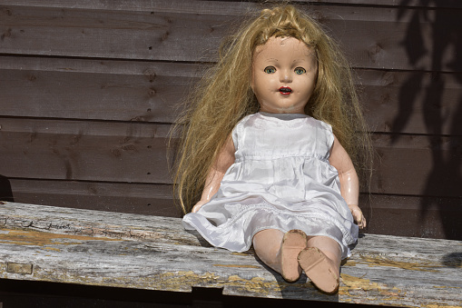 A closeup of a creepy old toy sitting on a weathered wooden surface