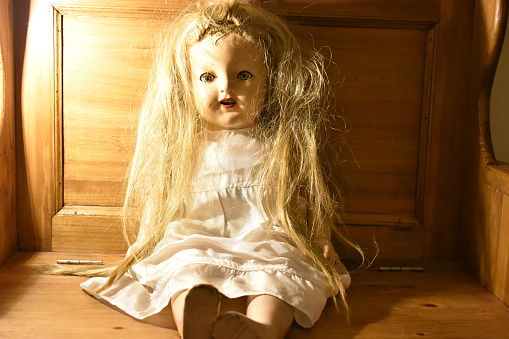 A closeup of a creepy old doll on the wooden chair