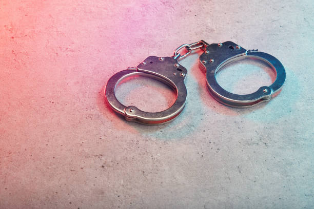 istock Handcuffs on concrete surface with police vehicle lighting 1464700360