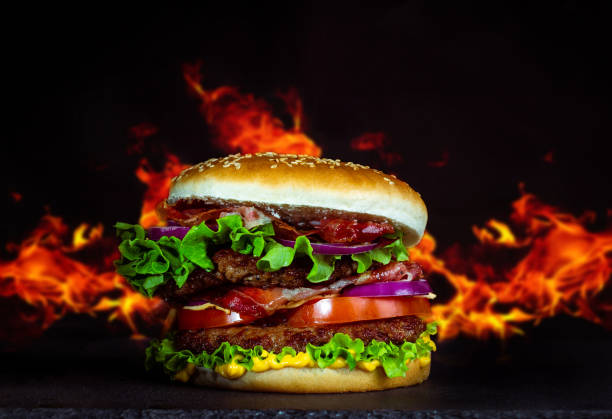 istock Closeup shot of an appetizing burger isolated on a black fire background 1464701362