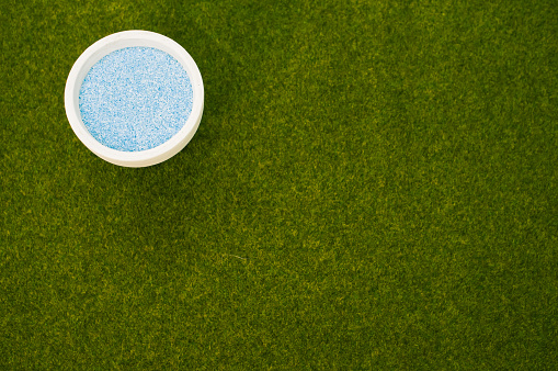 A top view of a white ornamental pot with blue sand on the grass with a copy space