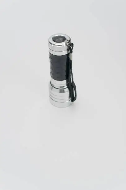 A vertical shot of a small black-silver flashlight isolated on a white background