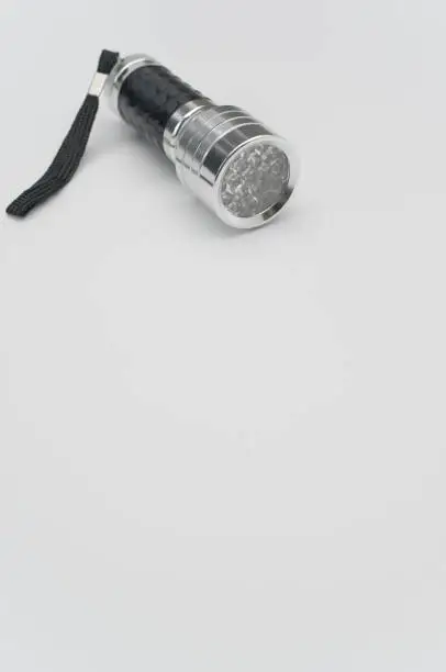 A vertical shot of a small black-silver flashlight isolated on a white background