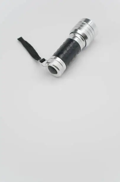 A vertical shot of a small black-silver flashlight isolated on a white background