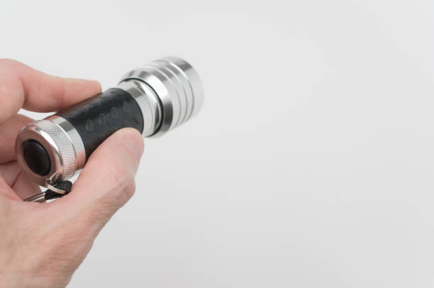 istock Hand of a male holding a small black-silver flashlight on a white background 1464704853