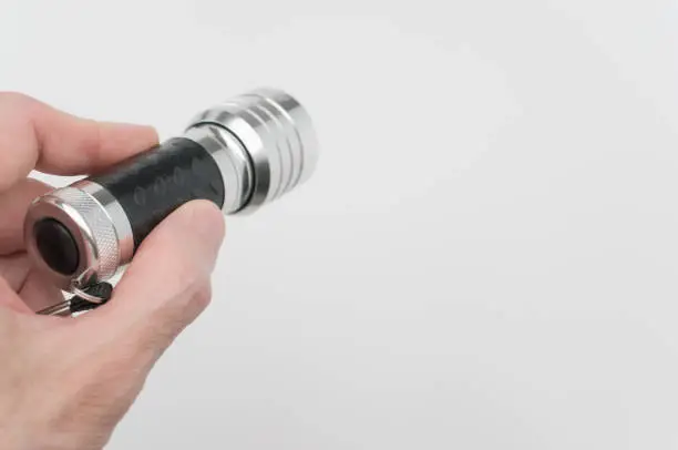 A hand of a male holding a small black-silver flashlight on a white background