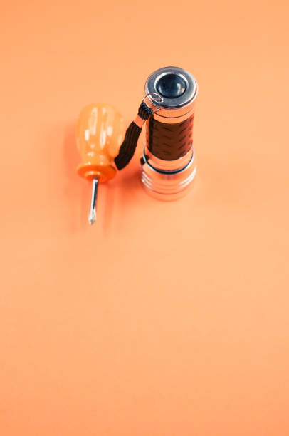 istock Vertical shot of a small screwdriver and flashlight isolated on an orange background 1464704859