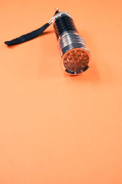 A vertical shot of a small black-silver flashlight isolated on an orange background