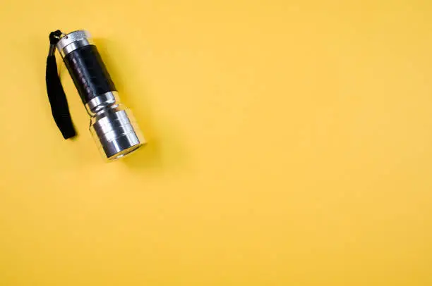 A top view of a small black-silver flashlight isolated on a yellow background