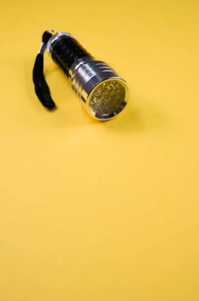 A vertical shot of a small black-silver flashlight isolated on a yellow background