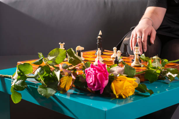 In the foreground is a table with a checkerboard and placed figures, two multi-colored roses. In the background, a female hand.