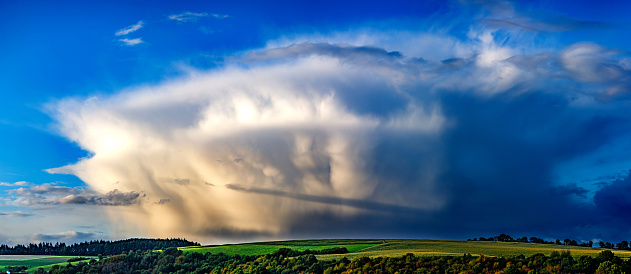 A thunderstorm cell over a green hill and forest
