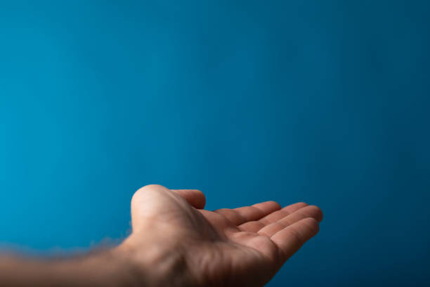 Closeup of a male shows outstretched hand isolated on a blue background A closeup of a male shows outstretched hand isolated on a blue background male is standing and shows outstretched hand with open palm stock pictures, royalty-free photos & images